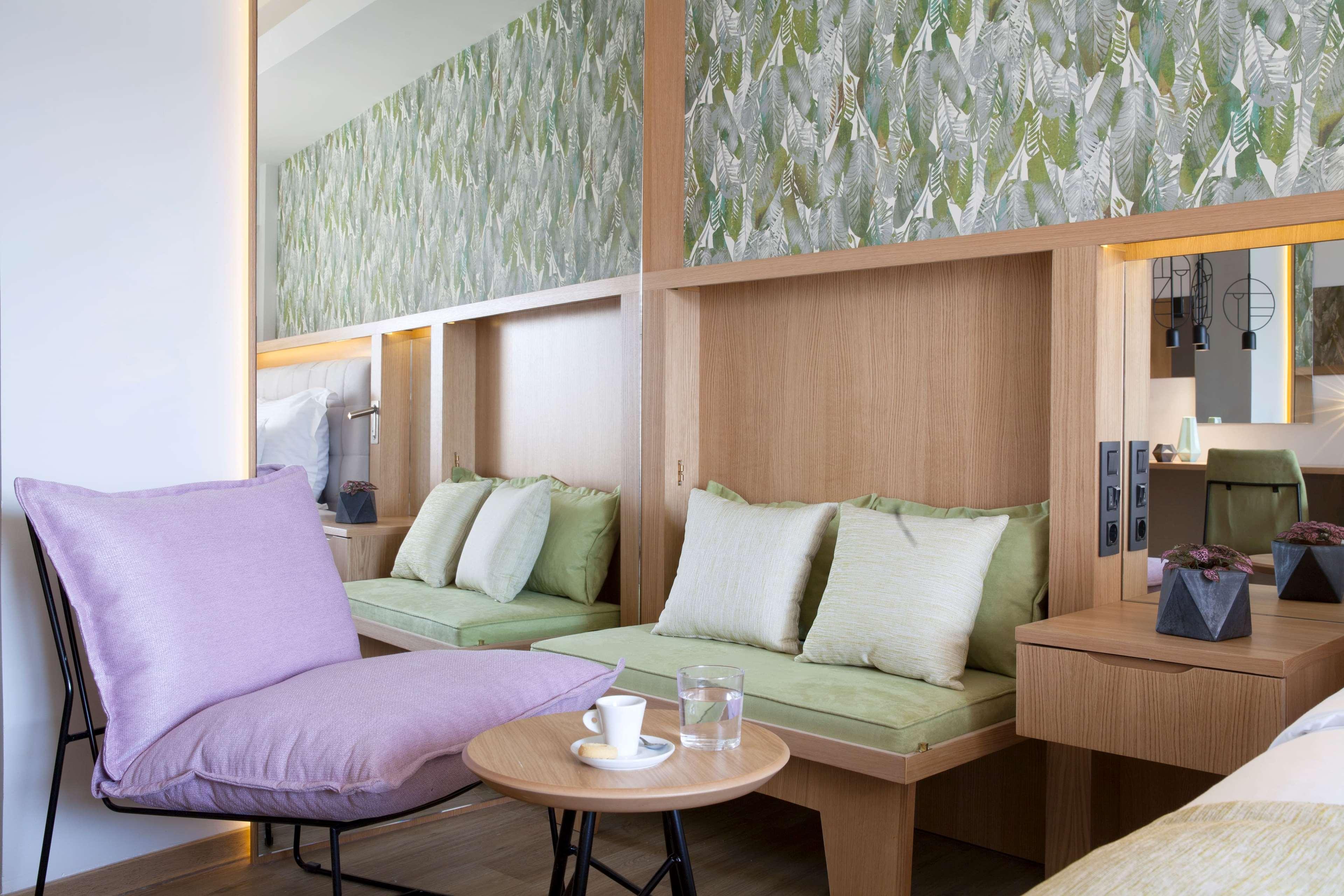Dolce By Wyndham Athens Attica Riviera Hotel Vravrona Luaran gambar The photo shows a modern interior design of a room or lounge area. There are built-in lounging spaces with green cushions against a wooden backdrop. The wall behind features a decorative pattern, possibly with a natural or leafy theme. In the foregro