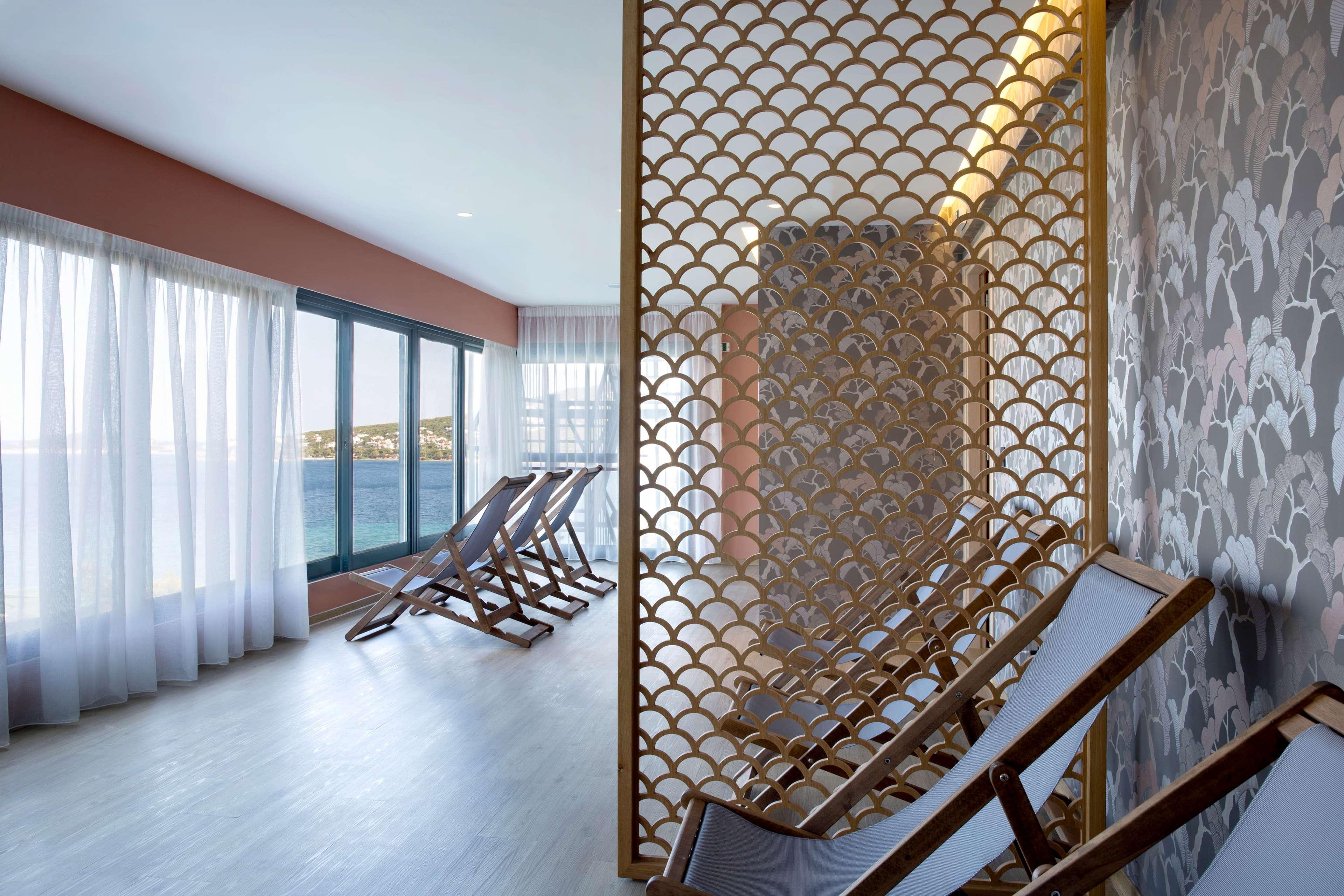 Dolce By Wyndham Athens Attica Riviera Hotel Vravrona Luaran gambar The photo shows a serene and stylish interior space, likely a lounge or relaxation area. There are several reclining chairs positioned near large windows that offer a view, possibly of the outdoors or a body of water. The space is divided by a decora