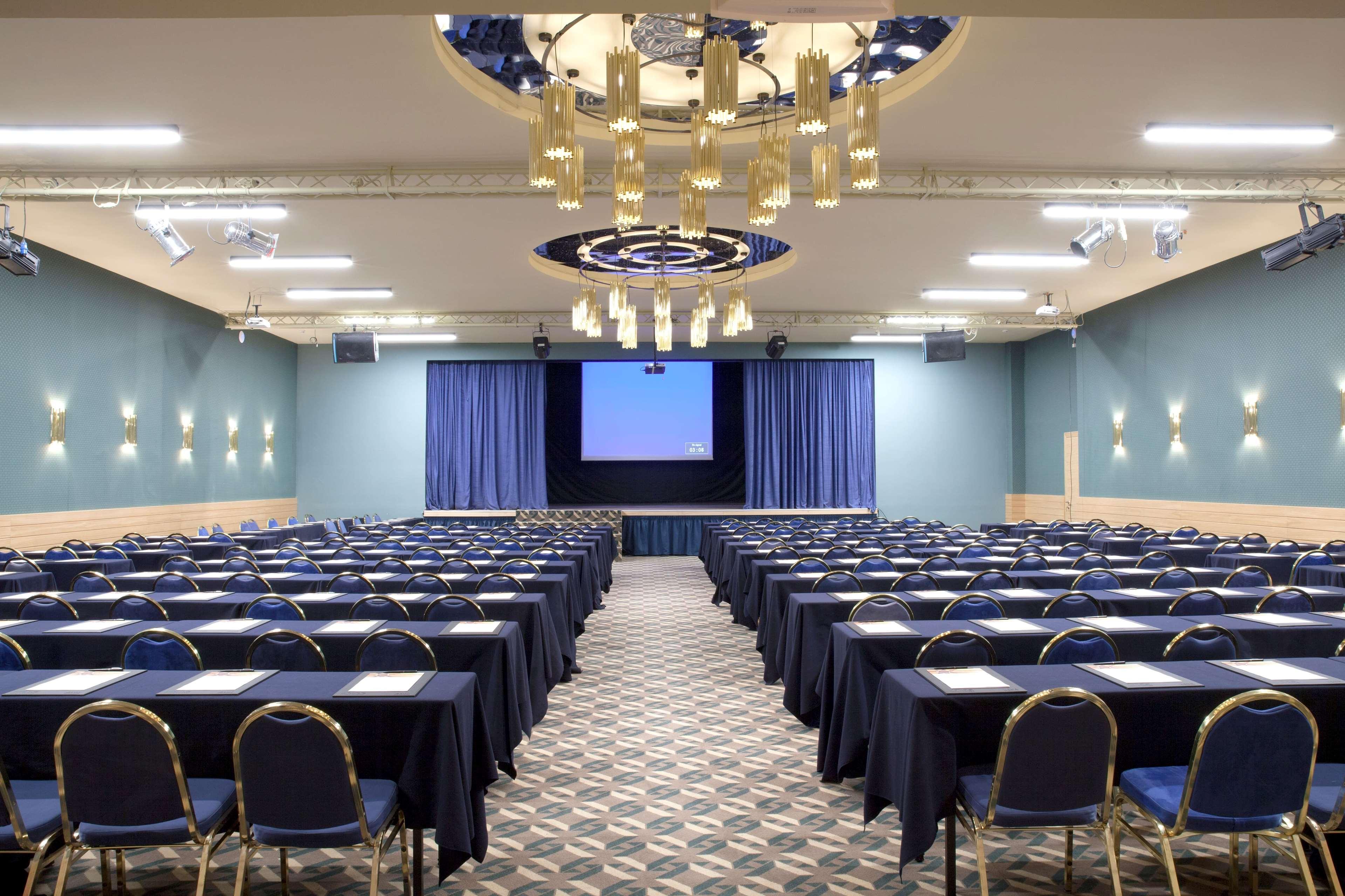 Dolce By Wyndham Athens Attica Riviera Hotel Vravrona Luaran gambar The photo shows a large conference or meeting room. It features multiple rows of tables arranged in a classroom style, with each table equipped with chairs. The room has a professional setup, indicated by dark tablecloths and notepads on each table. 