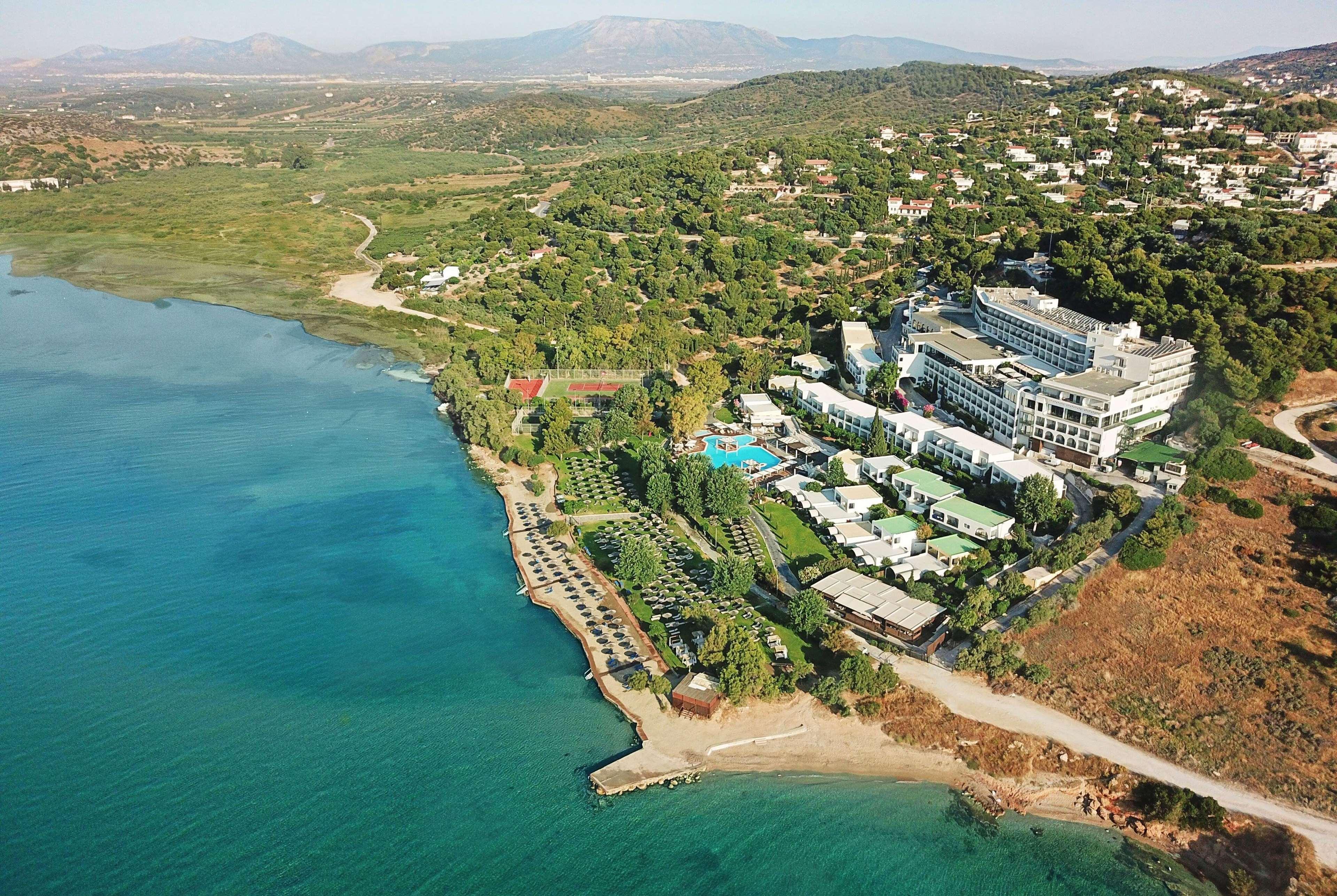 Dolce By Wyndham Athens Attica Riviera Hotel Vravrona Luaran gambar The photo shows an aerial view of a coastal area featuring a resort or hotel complex situated near the shoreline. The building has multiple levels and is surrounded by lush greenery and landscaped gardens. There is a pool area visible, as well as sev
