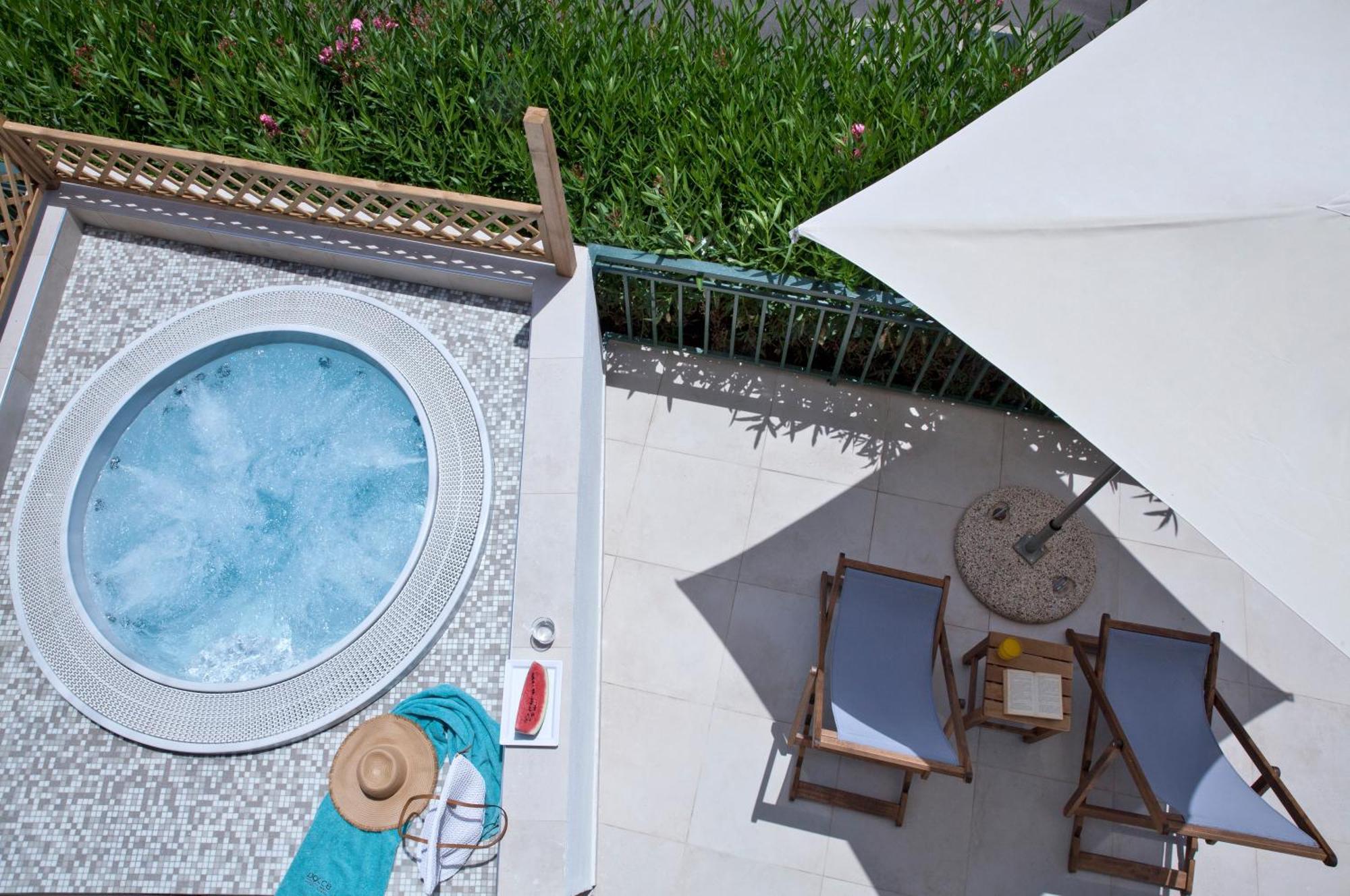 Dolce By Wyndham Athens Attica Riviera Hotel Vravrona Luaran gambar The photo shows an overhead view of a relaxing outdoor space. There's a round hot tub with light blue water and a decorative edge. Nearby, a couple of wooden lounge chairs are positioned underneath a large umbrella to provide shade. A small side tabl